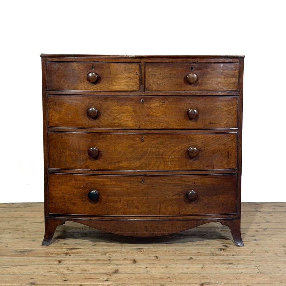 An antique Regency period mahogany bow-front chest of drawers featuring two short over three long graduated drawers with turned wooden handles.