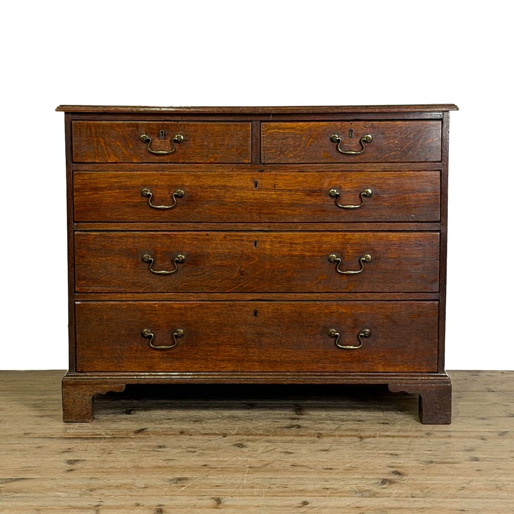 A Georgian oak chest of drawers featuring two short over three long graduated drawers, brass swan-neck handles, keyhole escutcheons, and bracket feet.