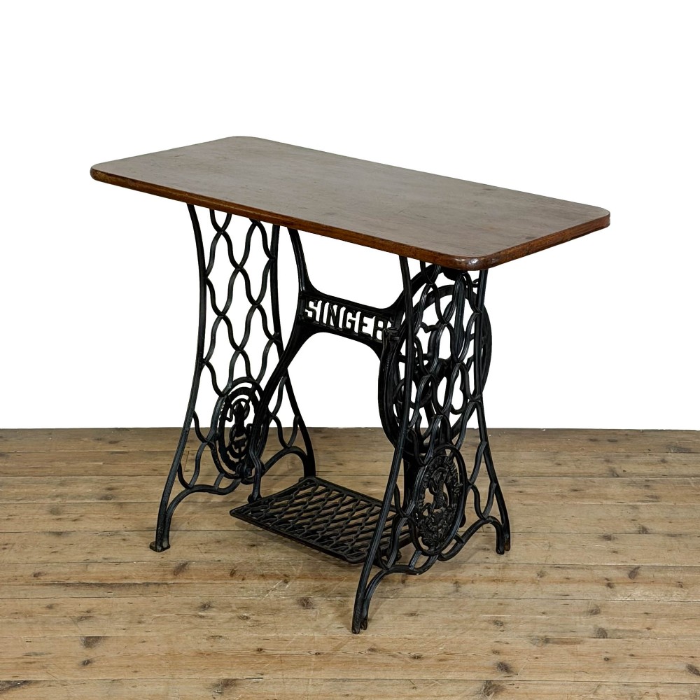 A black cast iron Singer treadle sewing machine base fitted with a flat rectangular wooden tabletop.