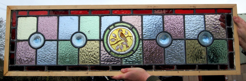 A colourful vibrant stained glass window with a painted bird centre