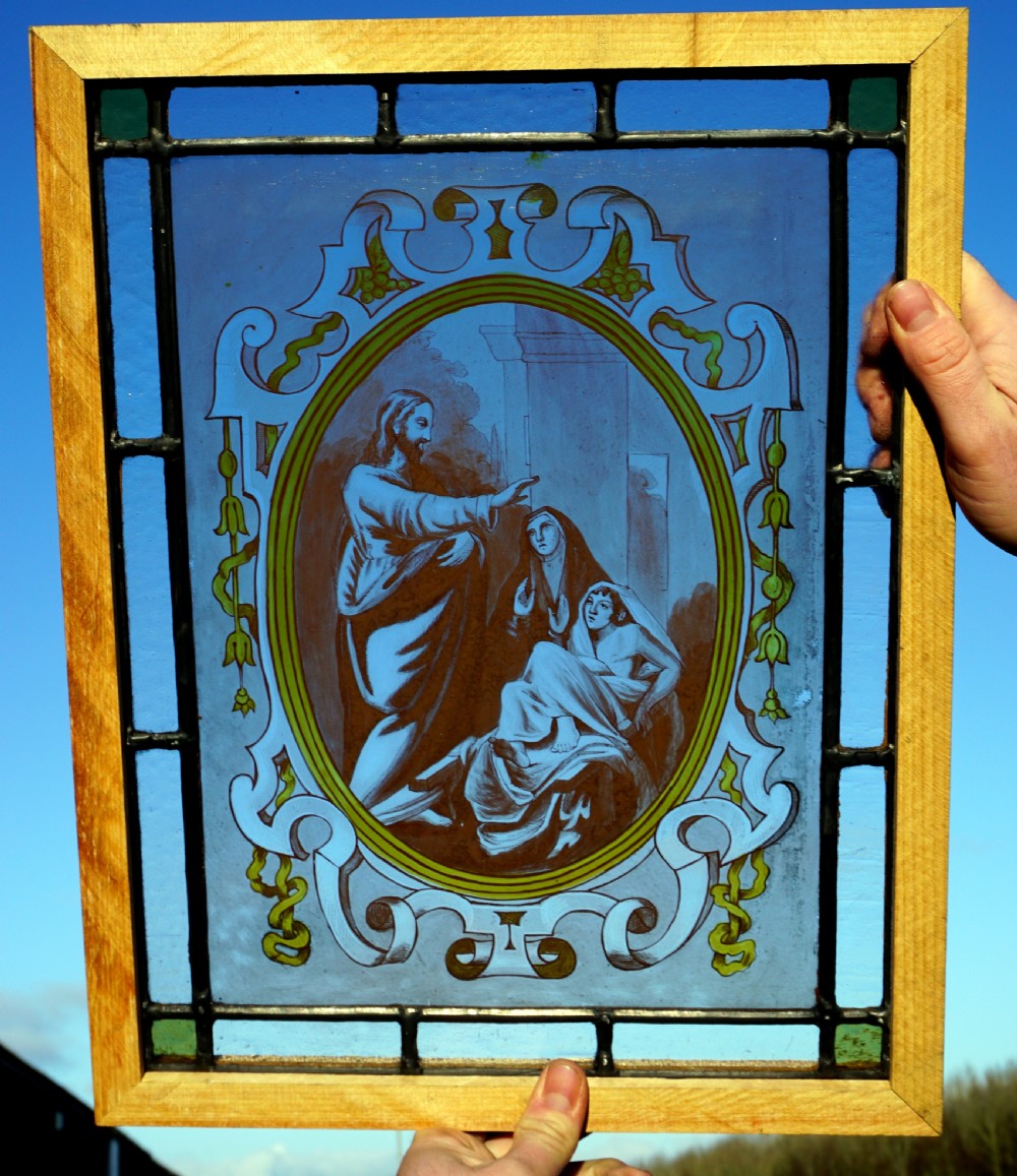 An antique rectangular stained glass panel featuring a central oval medallion with a hand-painted biblical scene surrounded by scrollwork in blue and yellow accents.