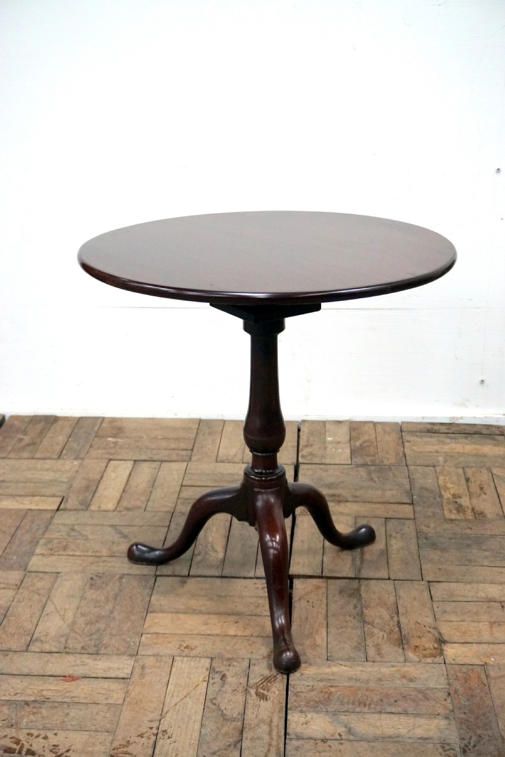 A Georgian mahogany tilt-top table featuring a circular top over a turned central stem and tripod cabriole legs with pad feet.