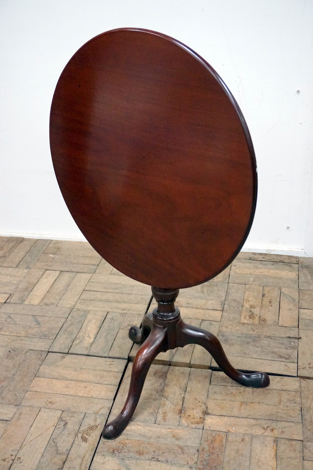 A Georgian mahogany tilt-top table featuring a circular top over a turned central stem and tripod cabriole legs with pad feet. View V