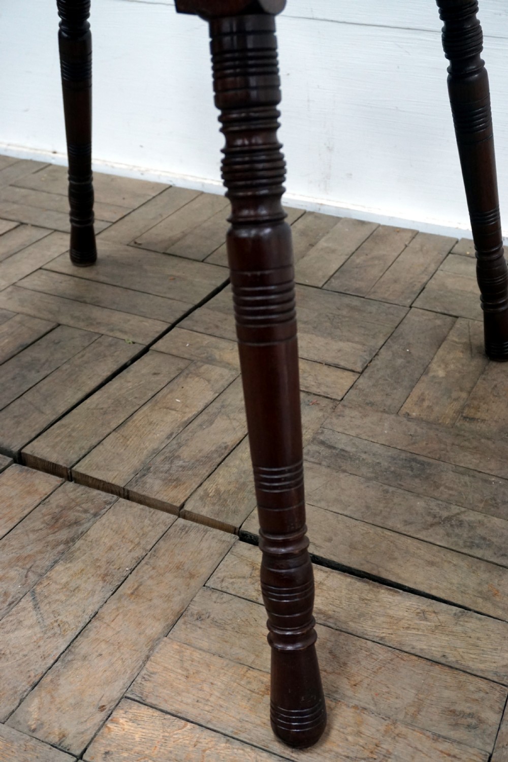 A square dark walnut coffee table featuring ring-turned legs and a shaped apron underneath. View V