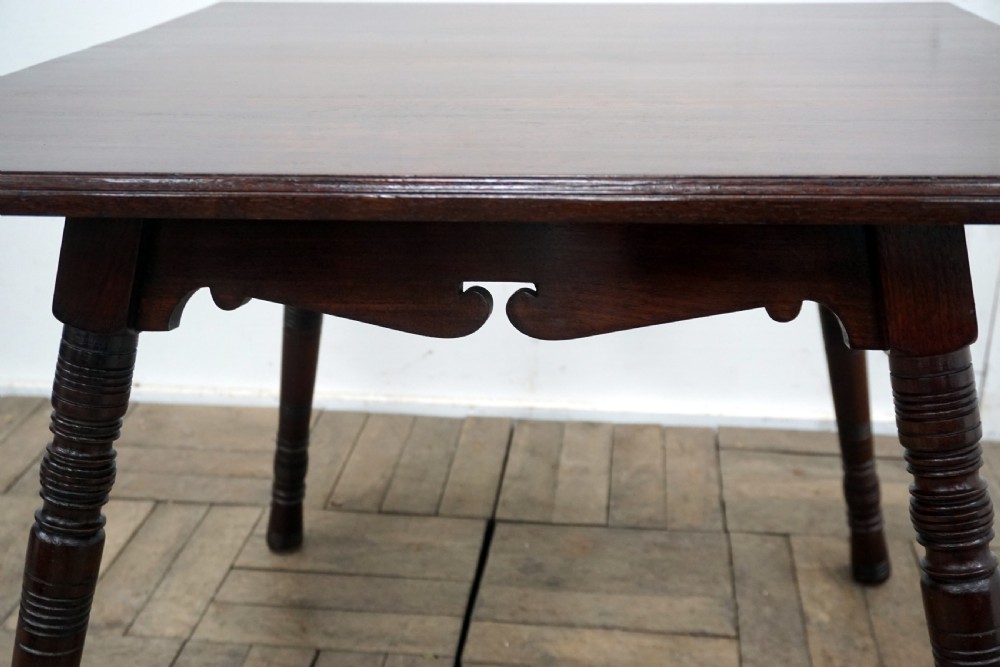 A square dark walnut coffee table featuring ring-turned legs and a shaped apron underneath. View VI