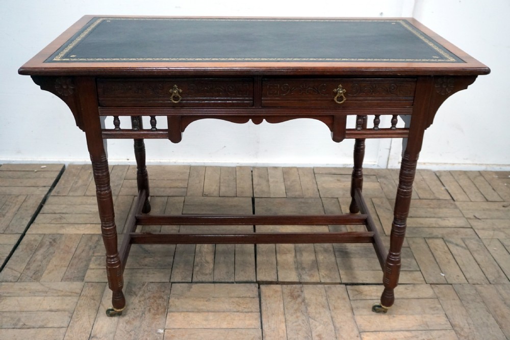 A Victorian mahogany writing desk featuring a green leather top, two carved front drawers with brass drop handles, turned legs, and brass castors.