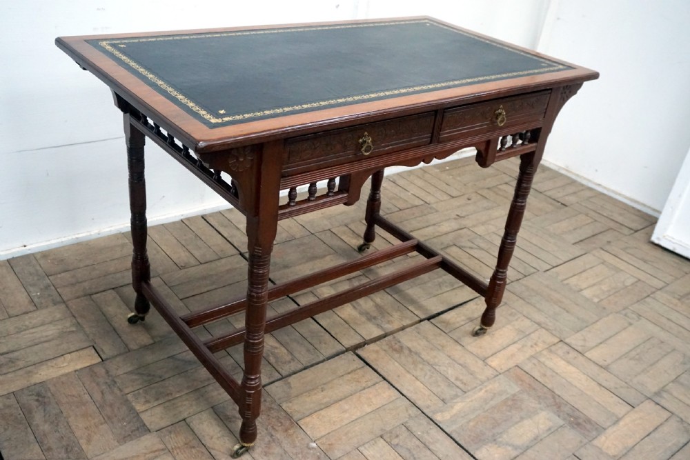 A Victorian mahogany writing desk featuring a green leather top, two carved front drawers with brass drop handles, turned legs, and brass castors. View II