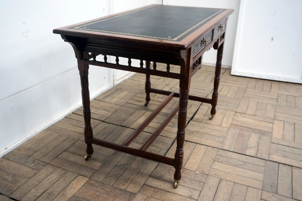 A Victorian mahogany writing desk featuring a green leather top, two carved front drawers with brass drop handles, turned legs, and brass castors. View III