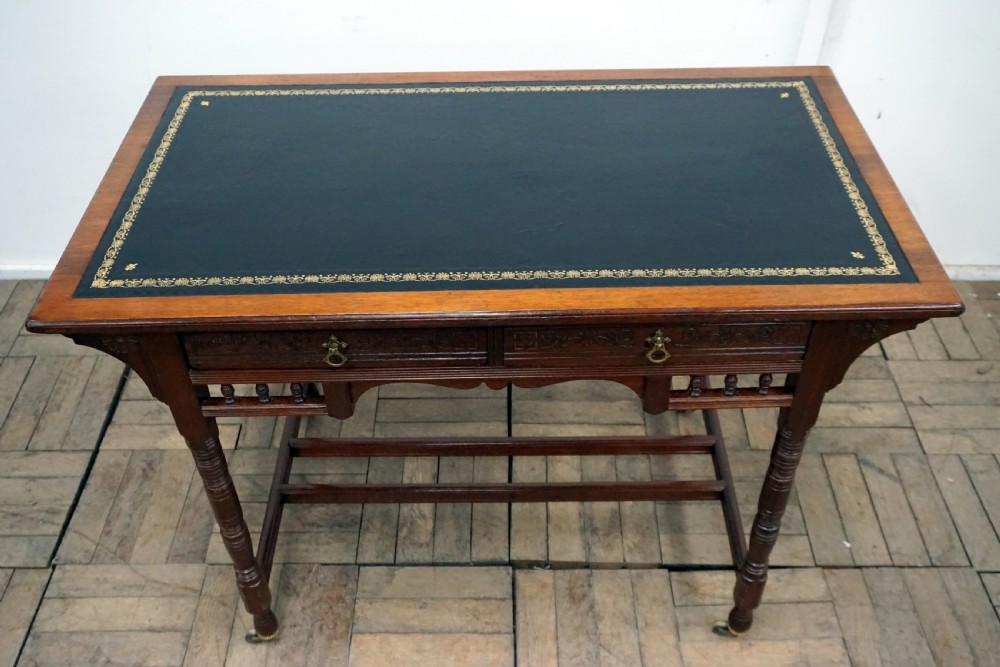 A Victorian mahogany writing desk featuring a green leather top, two carved front drawers with brass drop handles, turned legs, and brass castors. View IV