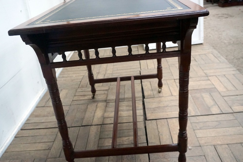 A Victorian mahogany writing desk featuring a green leather top, two carved front drawers with brass drop handles, turned legs, and brass castors. View V