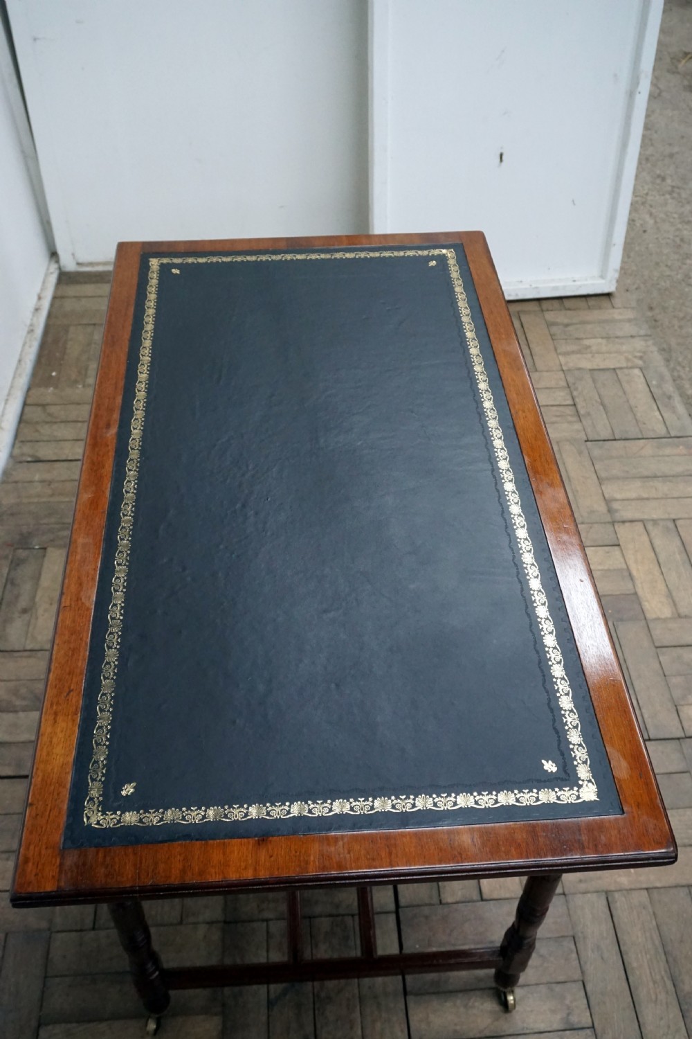 A Victorian mahogany writing desk featuring a green leather top, two carved front drawers with brass drop handles, turned legs, and brass castors. View VI