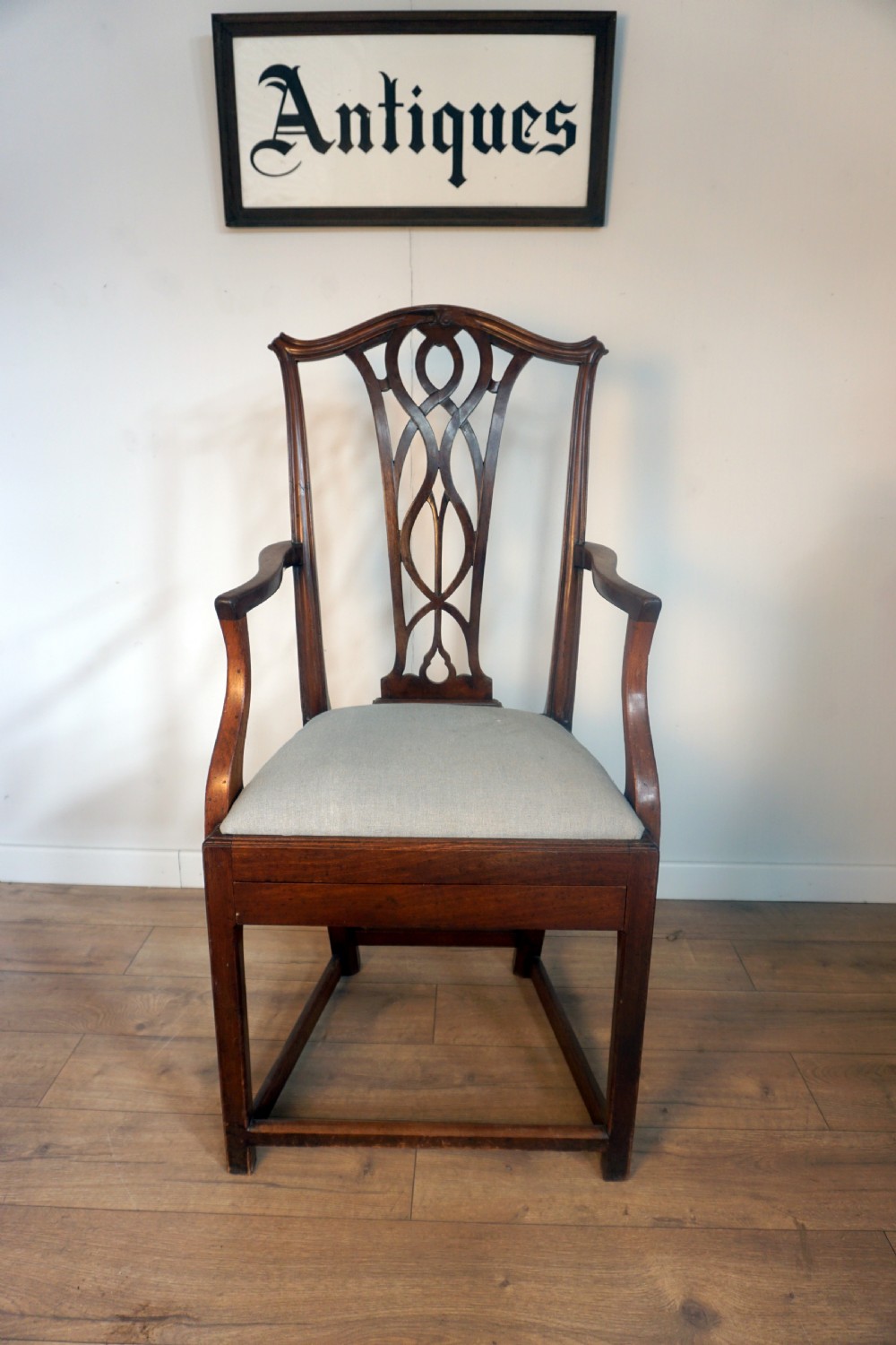A late Georgian dark mahogany carver armchair featuring a carved pierced splat back, shaped arms, and a light grey drop-in upholstered seat.