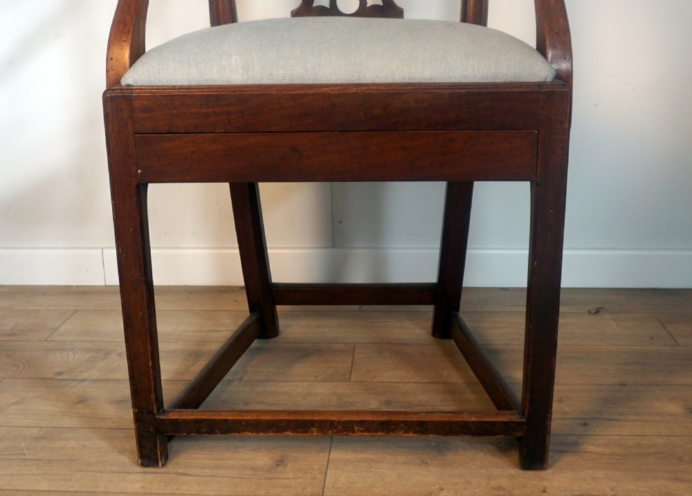 A late Georgian dark mahogany carver armchair featuring a carved pierced splat back, shaped arms, and a light grey drop-in upholstered seat. View V
