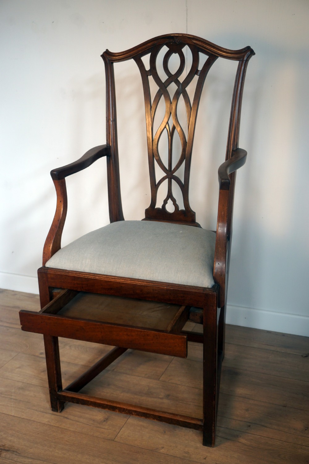 A late Georgian dark mahogany carver armchair featuring a carved pierced splat back, shaped arms, and a light grey drop-in upholstered seat. View VI