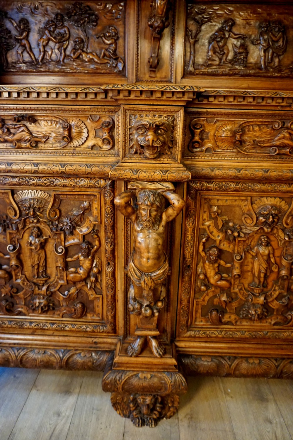 A two-tier carved wooden buffet featuring detailed relief panels of mythological scenes, carved putti, and supporting caryatid figures. View III