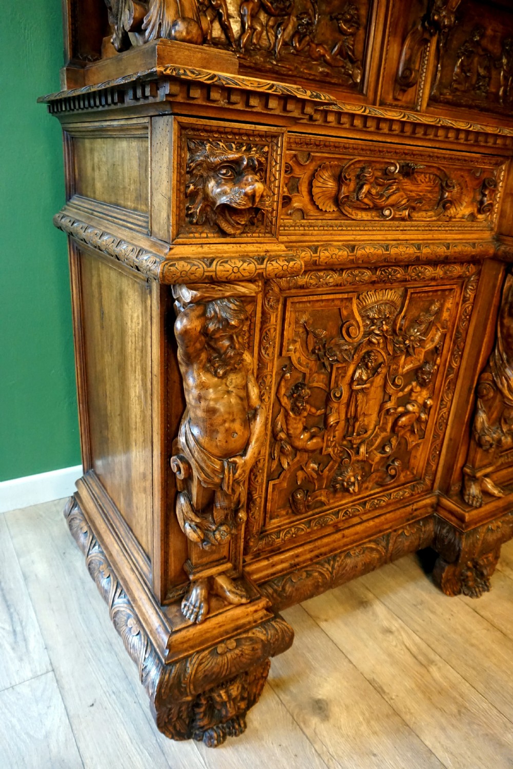 A two-tier carved wooden buffet featuring detailed relief panels of mythological scenes, carved putti, and supporting caryatid figures. View VI