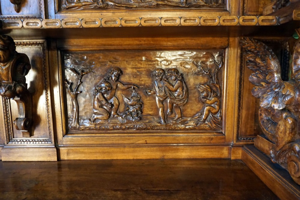 A two-tier carved wooden buffet featuring detailed relief panels of mythological scenes, carved putti, and supporting caryatid figures. View VII