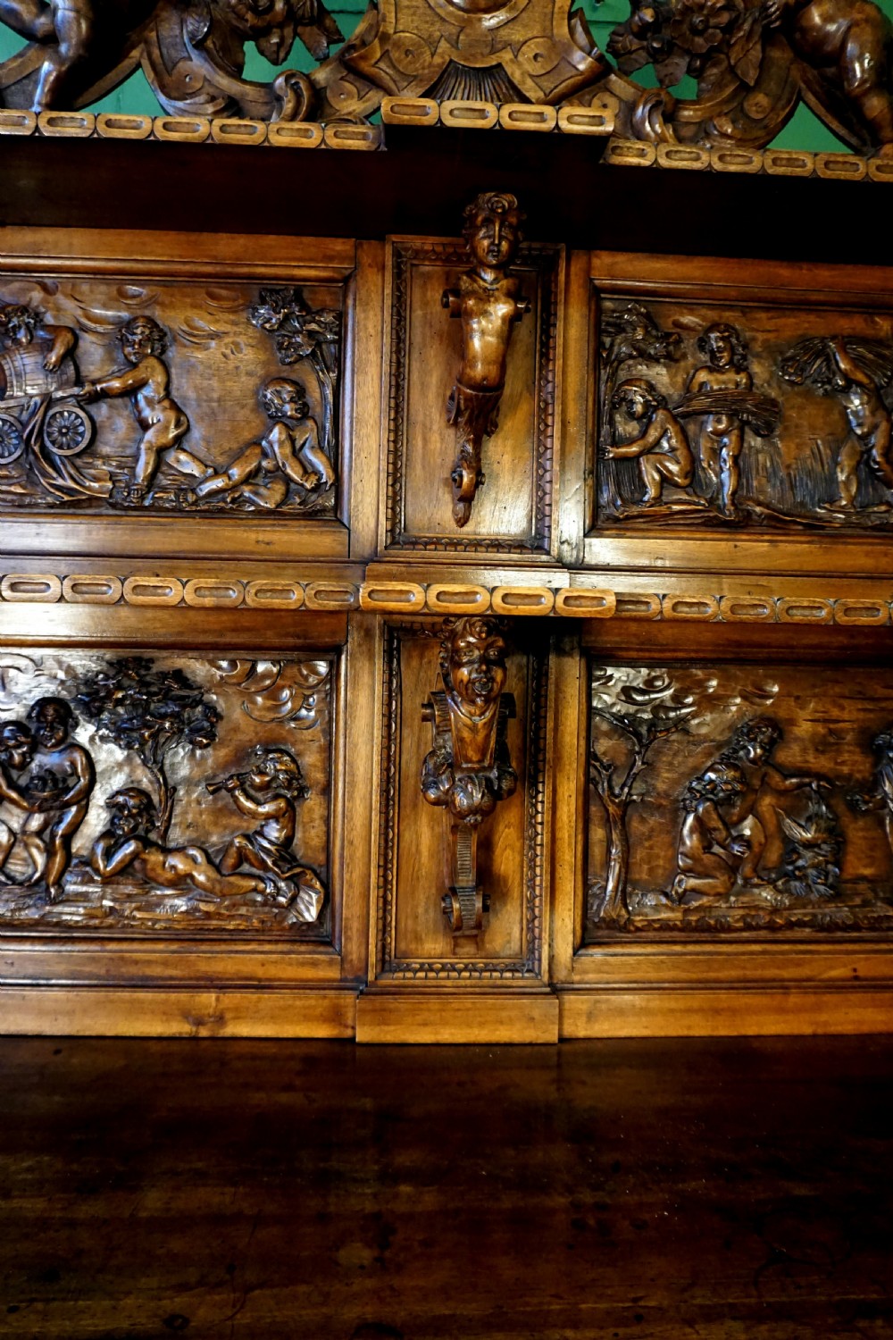 A two-tier carved wooden buffet featuring detailed relief panels of mythological scenes, carved putti, and supporting caryatid figures. View IX