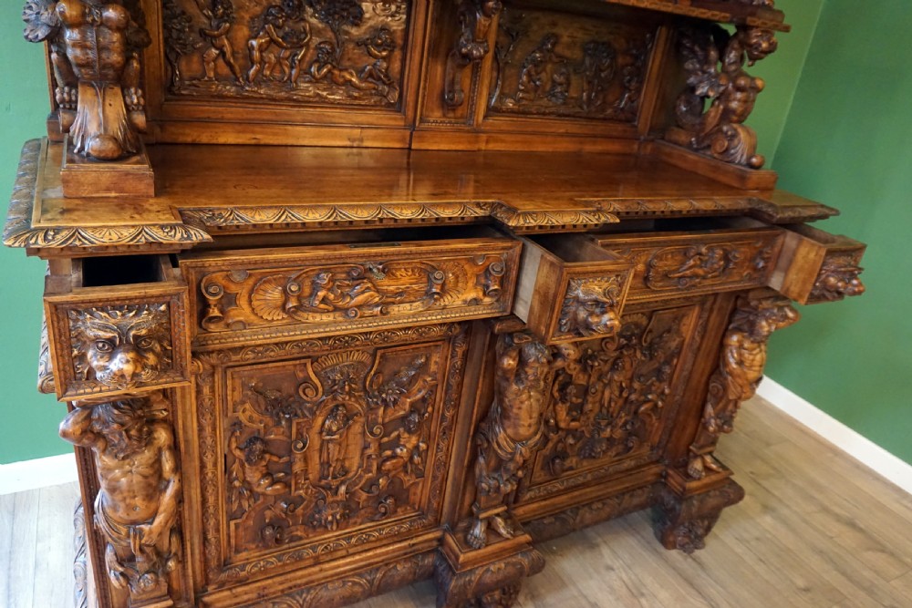 A two-tier carved wooden buffet featuring detailed relief panels of mythological scenes, carved putti, and supporting caryatid figures. View XIII