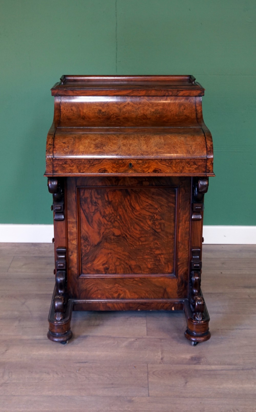 A Victorian burr walnut piano top davenport desk featuring scroll carved supports, side drawers, and a curved writing top section. View II