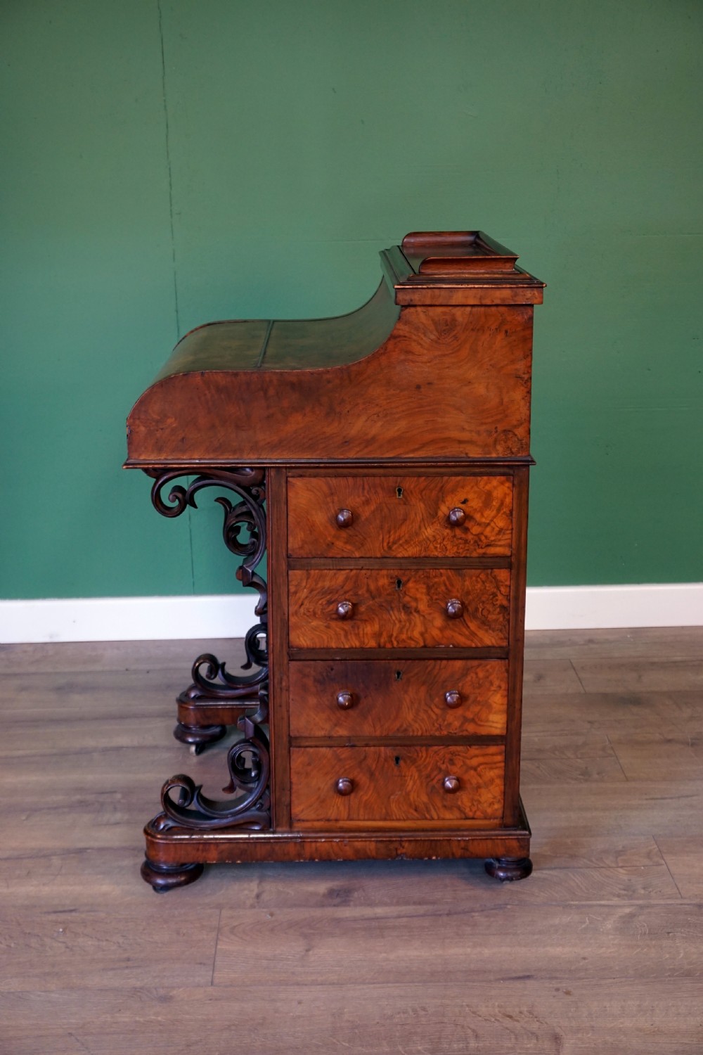A Victorian burr walnut piano top davenport desk featuring scroll carved supports, side drawers, and a curved writing top section. View III