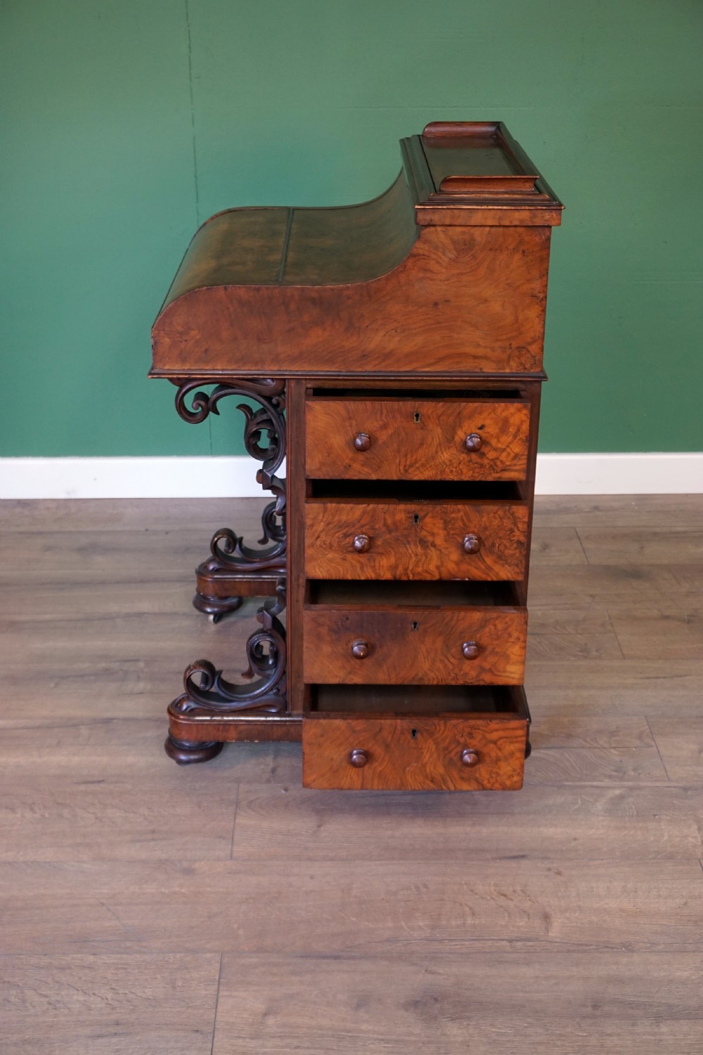 A Victorian burr walnut piano top davenport desk featuring scroll carved supports, side drawers, and a curved writing top section. View IV