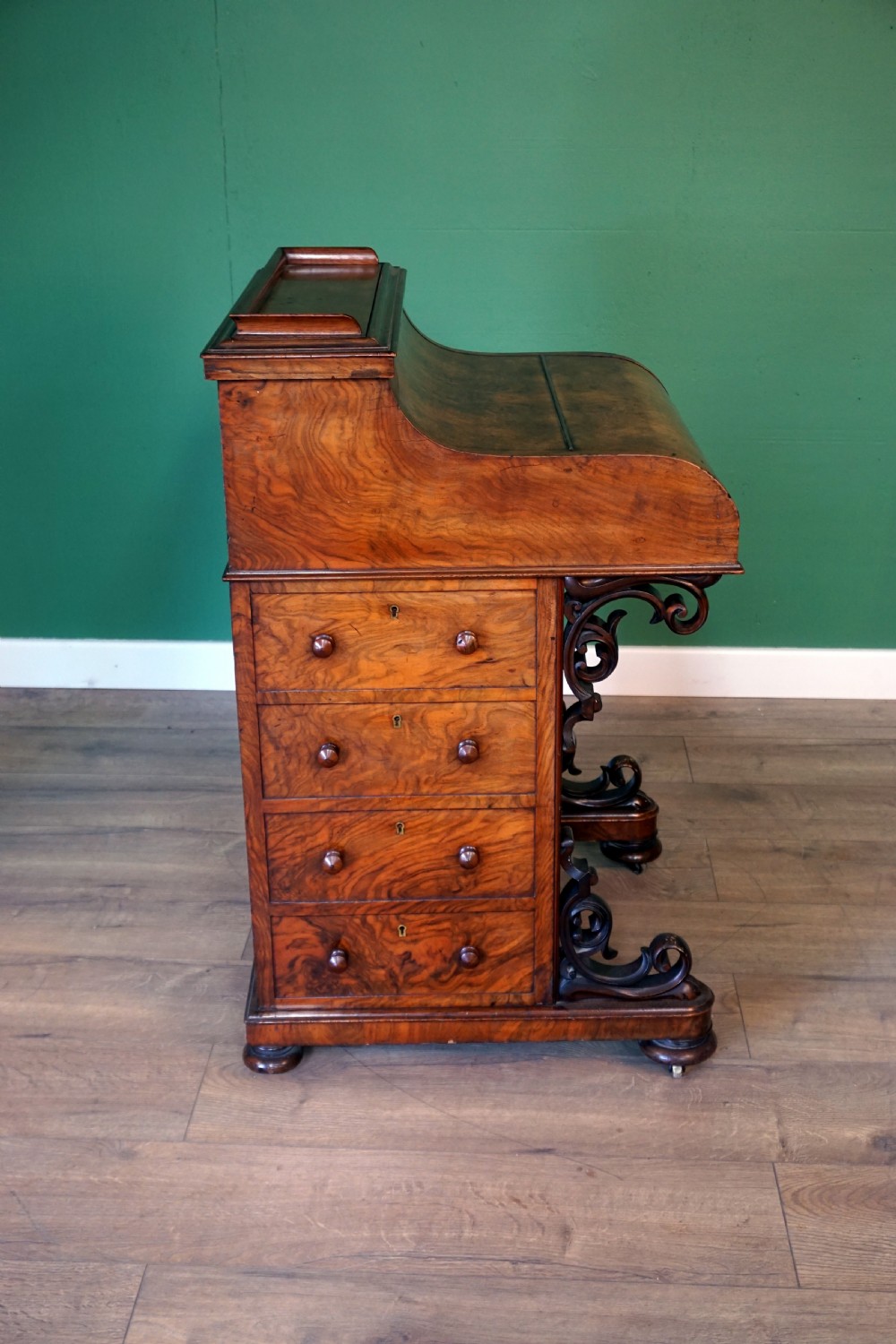 A Victorian burr walnut piano top davenport desk featuring scroll carved supports, side drawers, and a curved writing top section. View VI