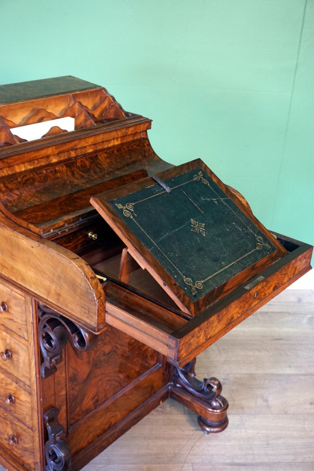 A Victorian burr walnut piano top davenport desk featuring scroll carved supports, side drawers, and a curved writing top section. View X