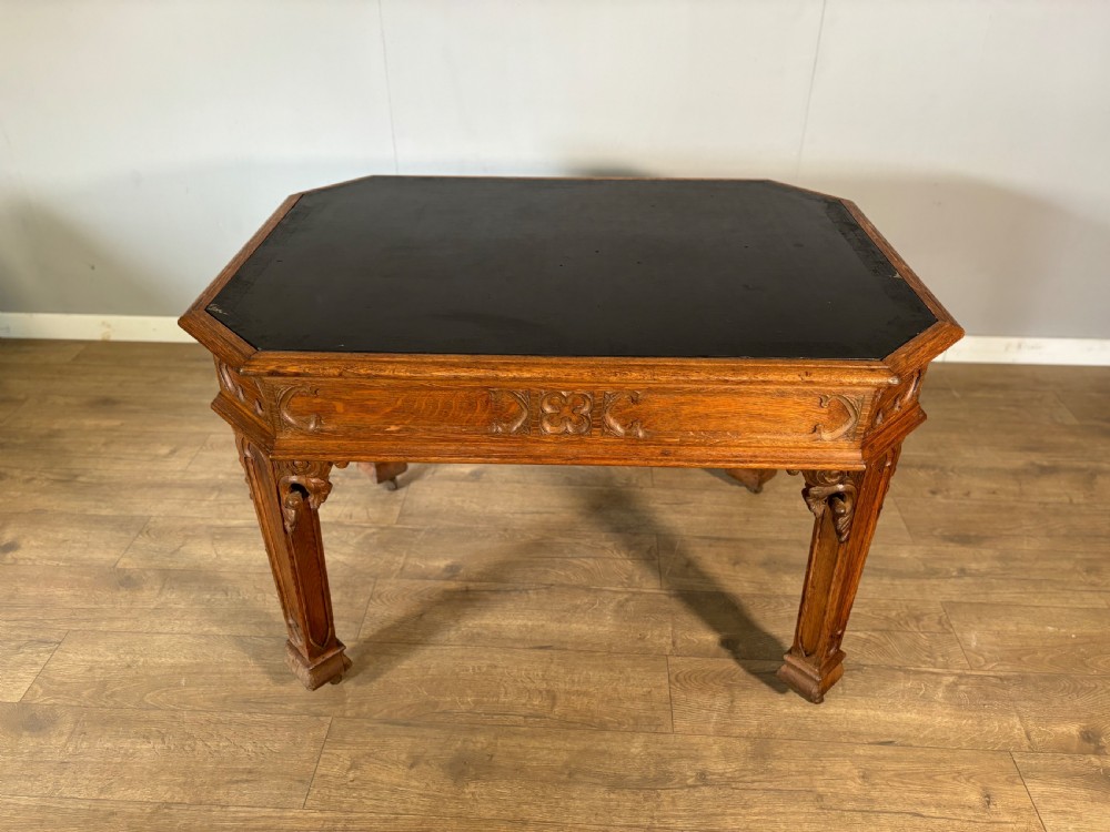 A Victorian Gothic Revival oak writing table featuring a dark leather inset top, carved quatrefoil frieze details, and detailed corner legs on castors. View II