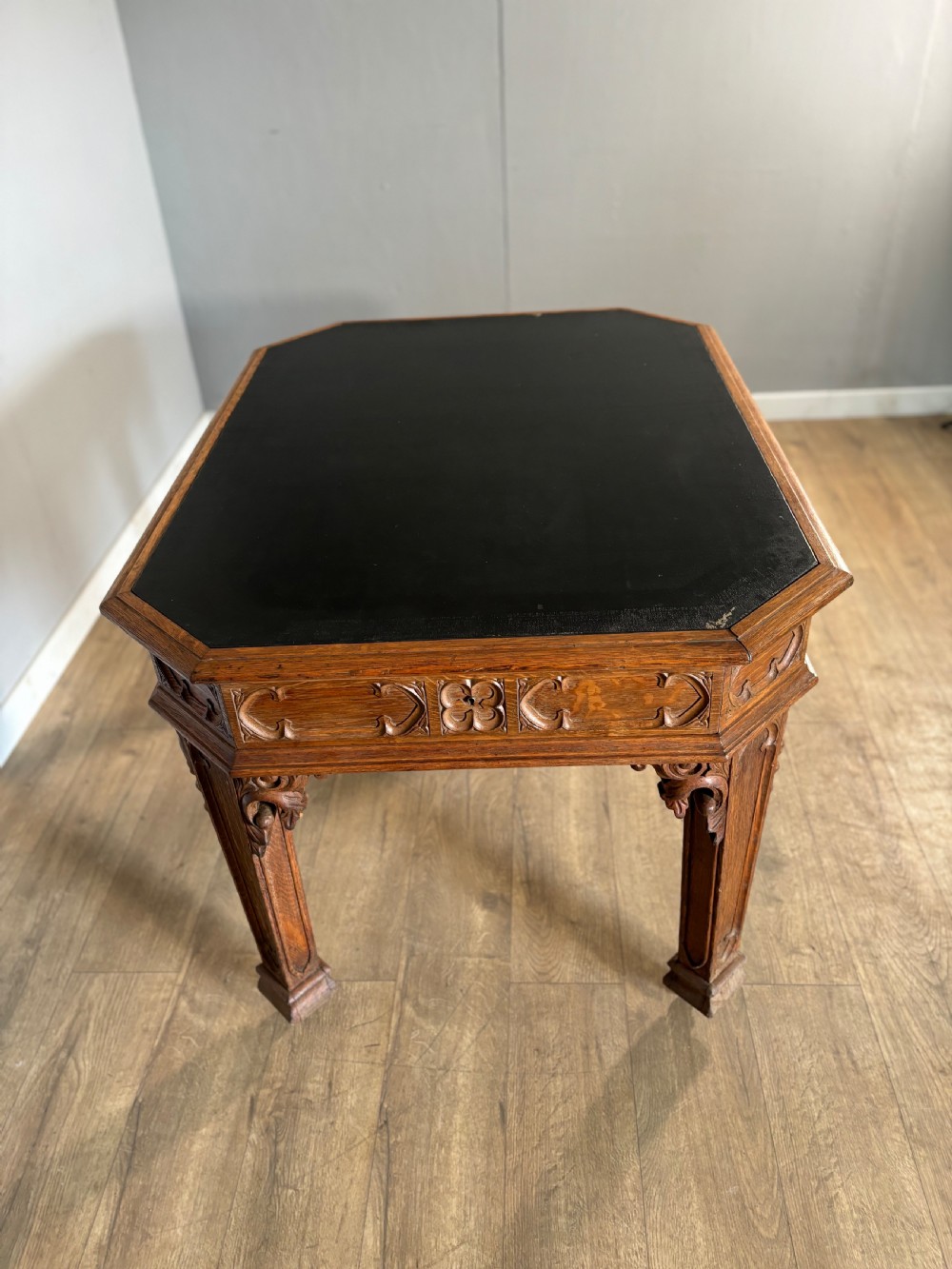 A Victorian Gothic Revival oak writing table featuring a dark leather inset top, carved quatrefoil frieze details, and detailed corner legs on castors. View IV