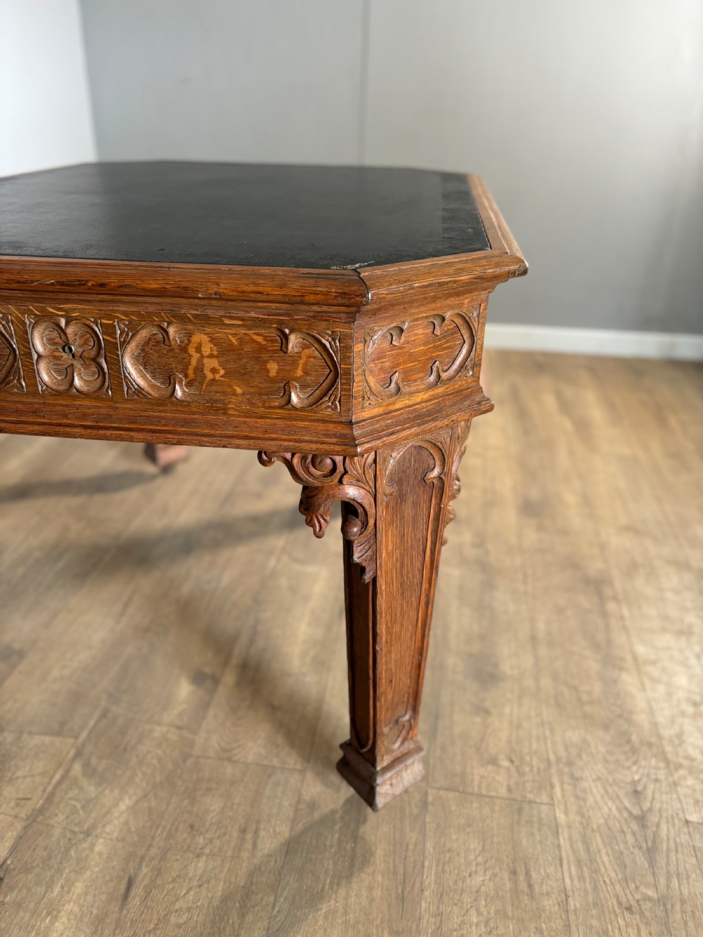 A Victorian Gothic Revival oak writing table featuring a dark leather inset top, carved quatrefoil frieze details, and detailed corner legs on castors. View VI