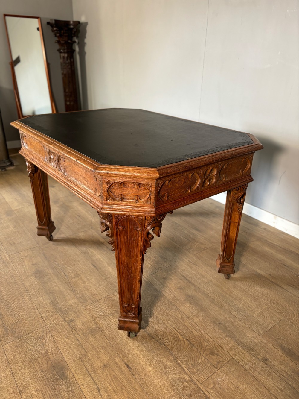 A Victorian Gothic Revival oak writing table featuring a dark leather inset top, carved quatrefoil frieze details, and detailed corner legs on castors. View VII