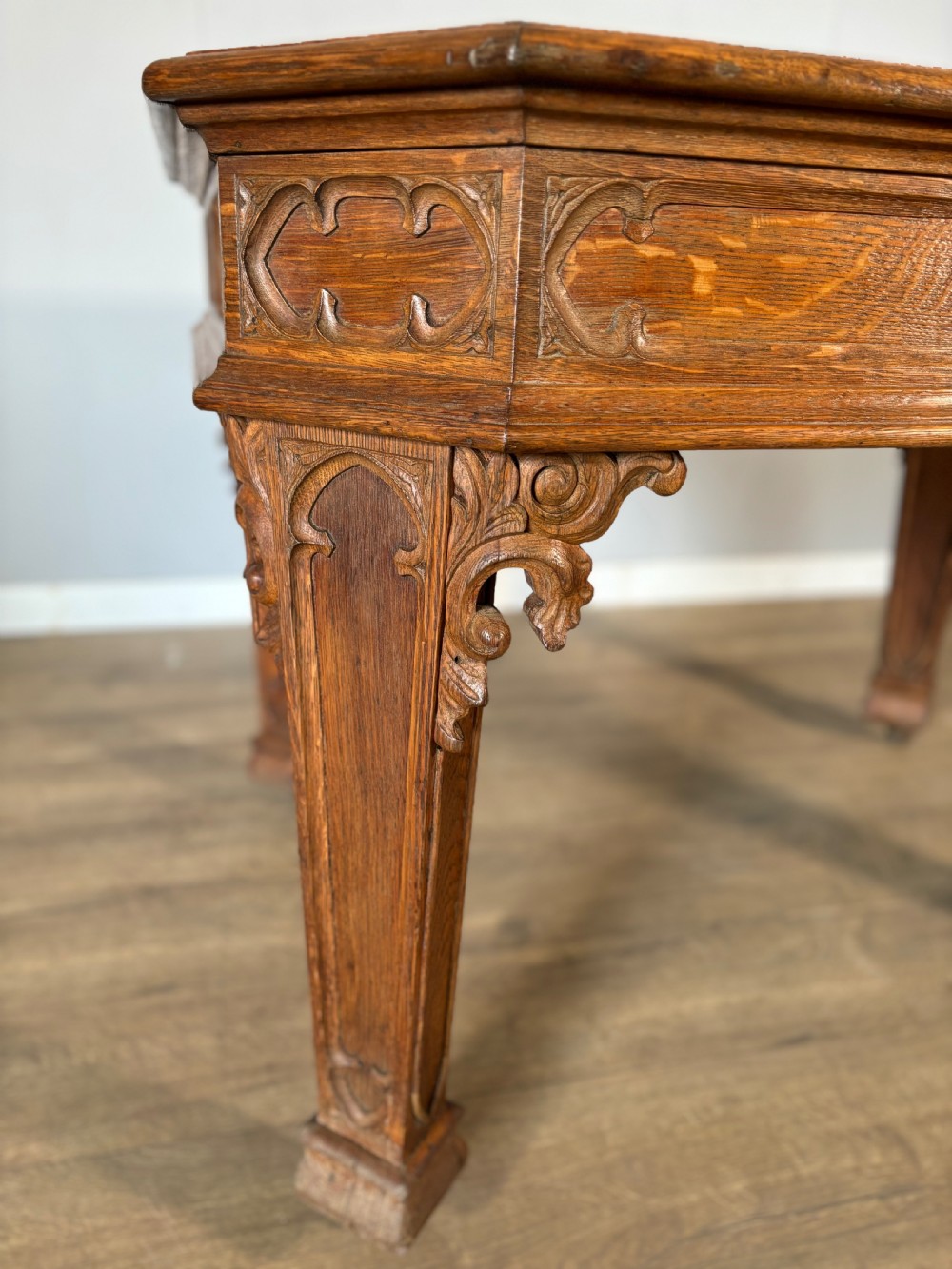 A Victorian Gothic Revival oak writing table featuring a dark leather inset top, carved quatrefoil frieze details, and detailed corner legs on castors. View VIII