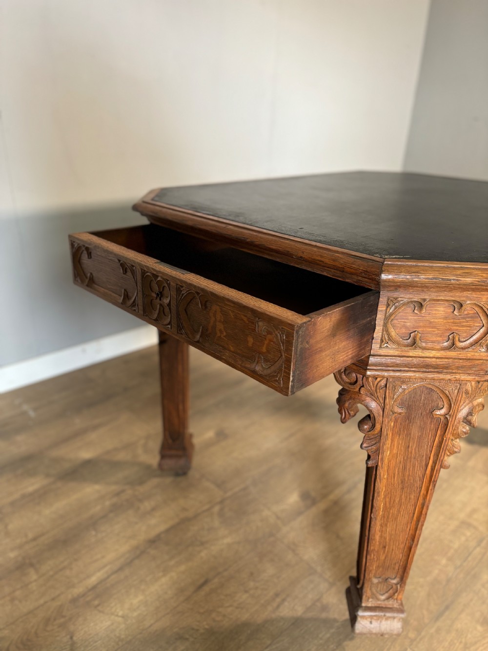 A Victorian Gothic Revival oak writing table featuring a dark leather inset top, carved quatrefoil frieze details, and detailed corner legs on castors. View XI