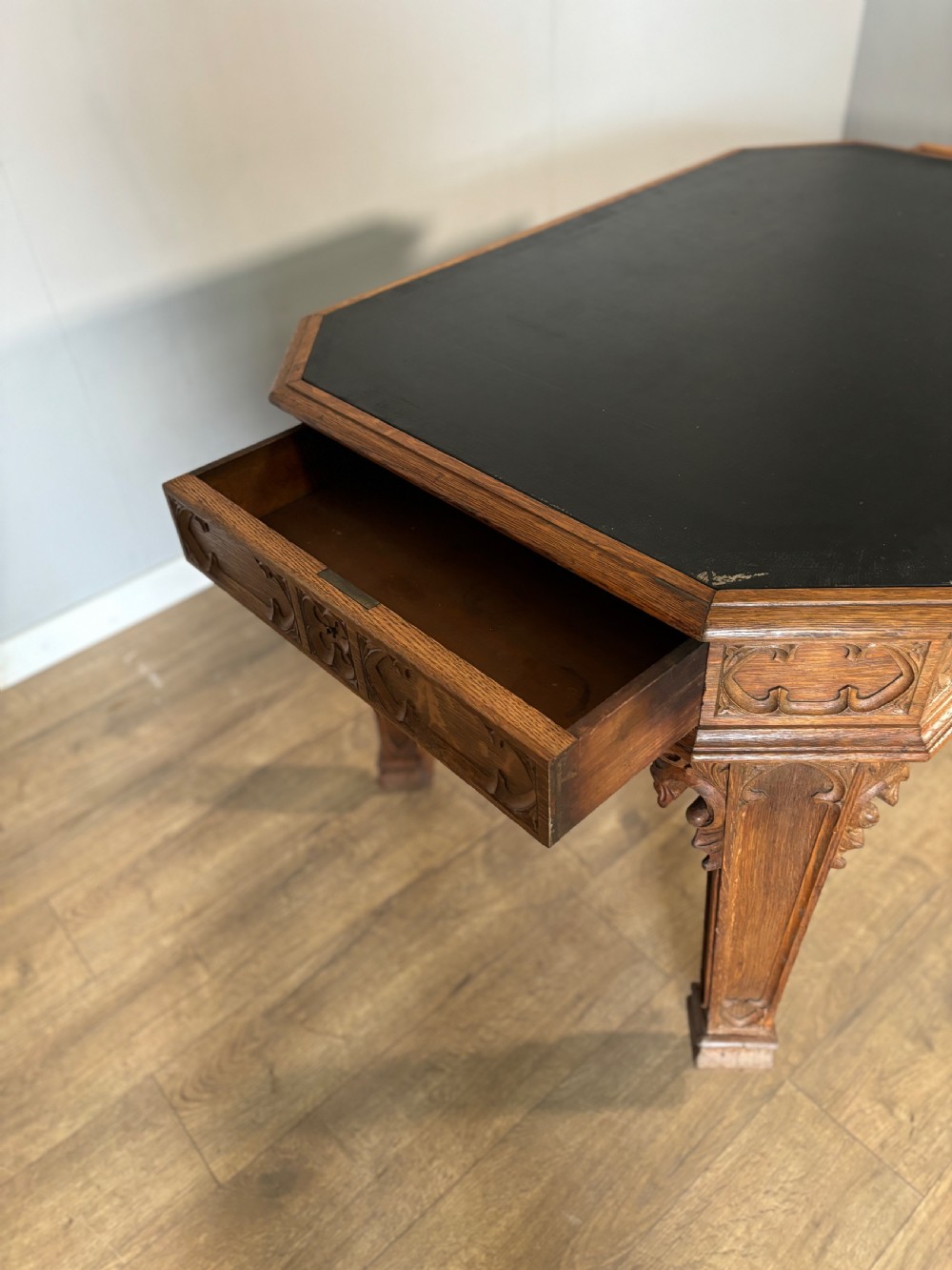 A Victorian Gothic Revival oak writing table featuring a dark leather inset top, carved quatrefoil frieze details, and detailed corner legs on castors. View XII