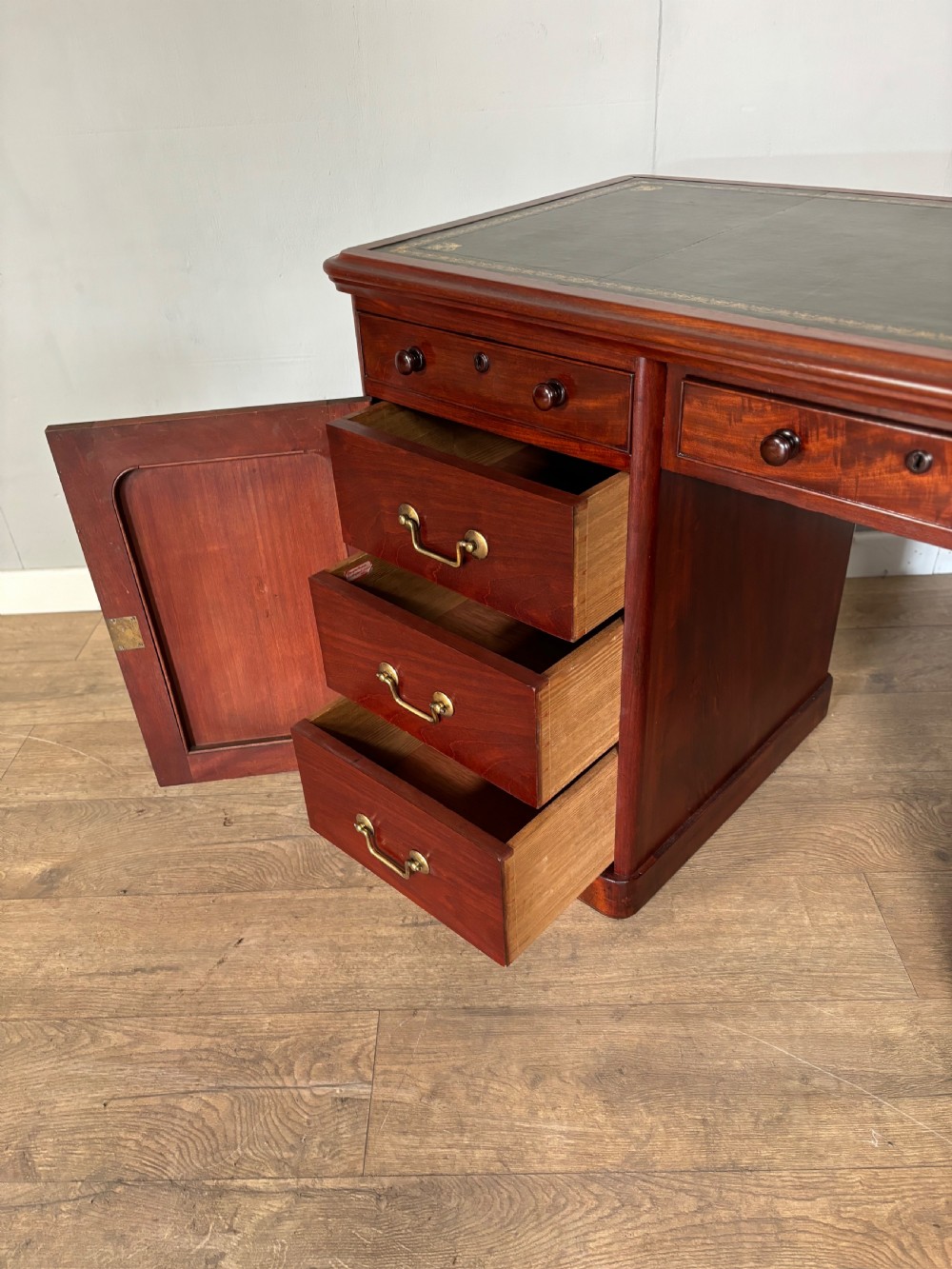 Victorian mahogany kneehole desk featuring a dark green leather writing surface, central frieze drawer, turned wooden knobs, and two cupboard pedestals with flame mahogany veneer panels. View VIII
