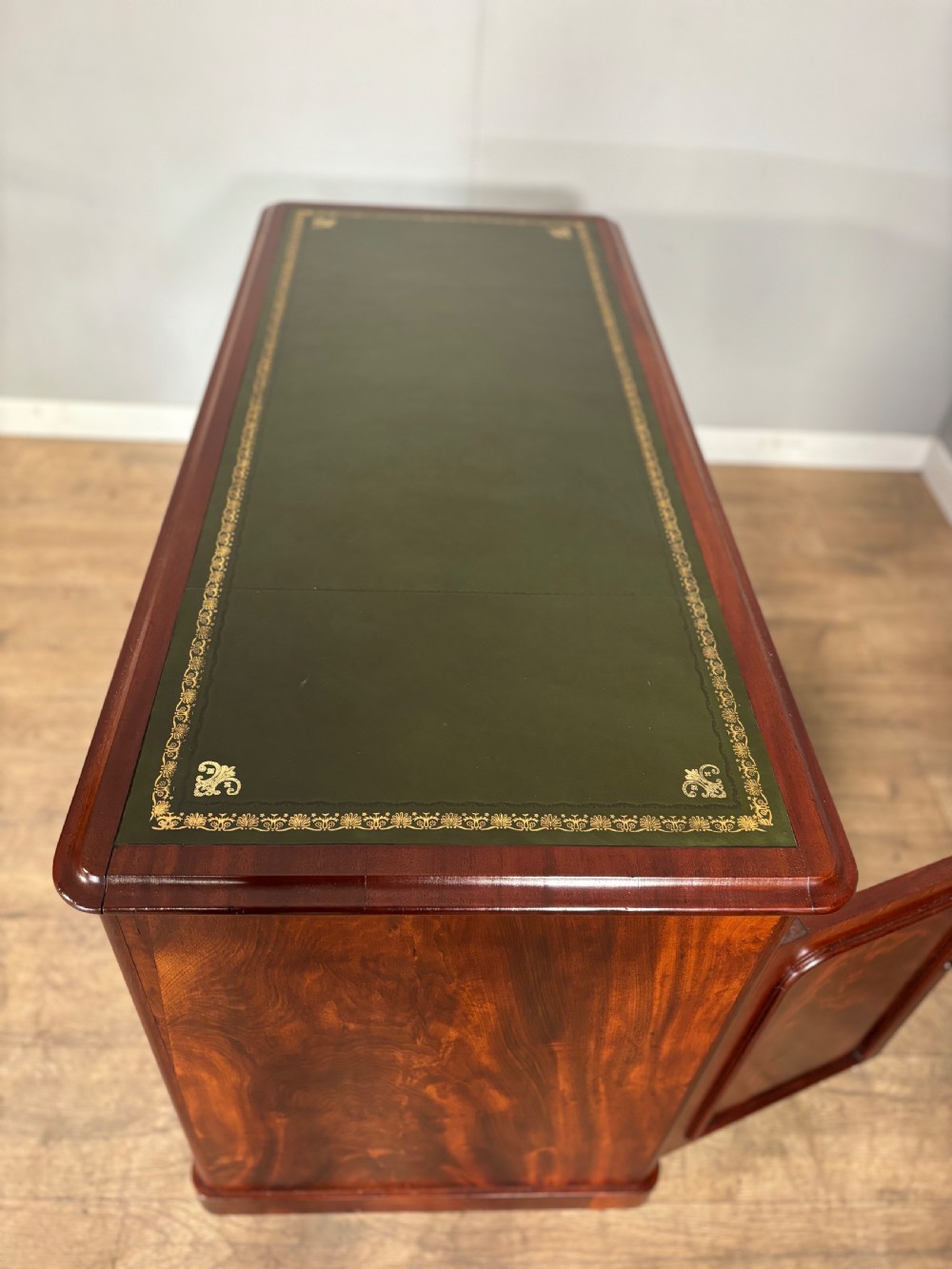 Victorian mahogany kneehole desk featuring a dark green leather writing surface, central frieze drawer, turned wooden knobs, and two cupboard pedestals with flame mahogany veneer panels. View X
