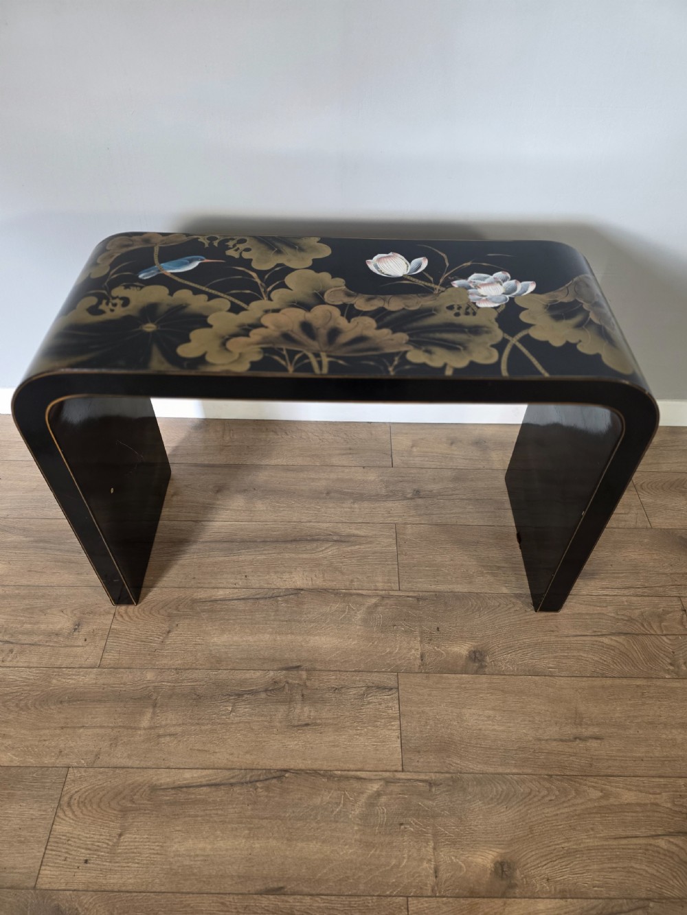 A mid-century black lacquered console table with rounded waterfall edges paired with a matching rectangular wall mirror decorated with hand-painted gold lotus leaves. View V