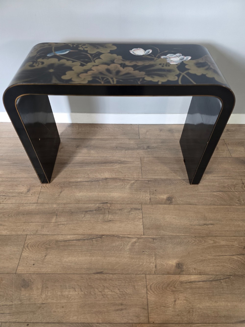 A mid-century black lacquered console table with rounded waterfall edges paired with a matching rectangular wall mirror decorated with hand-painted gold lotus leaves. View II