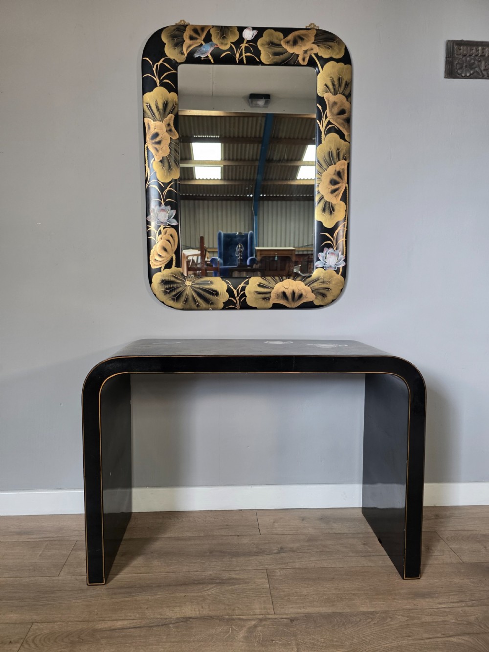 A mid-century black lacquered console table with rounded waterfall edges paired with a matching rectangular wall mirror decorated with hand-painted gold lotus leaves.