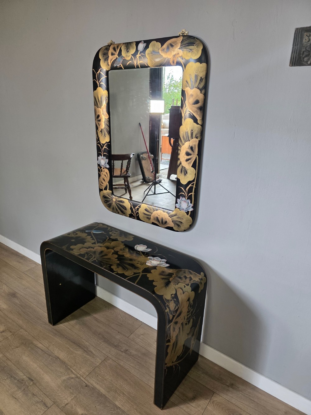 A mid-century black lacquered console table with rounded waterfall edges paired with a matching rectangular wall mirror decorated with hand-painted gold lotus leaves. View IX