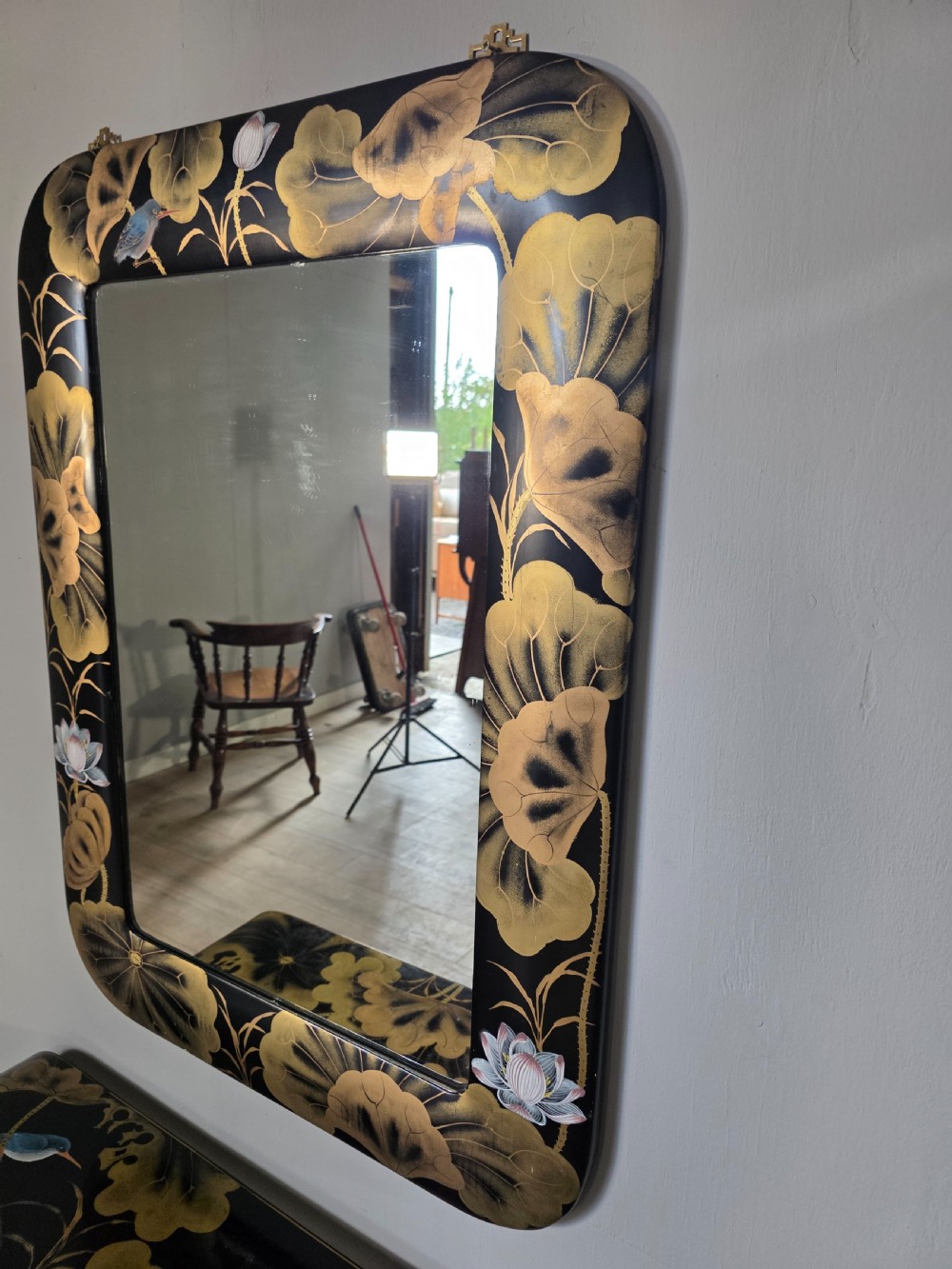 A mid-century black lacquered console table with rounded waterfall edges paired with a matching rectangular wall mirror decorated with hand-painted gold lotus leaves. View X