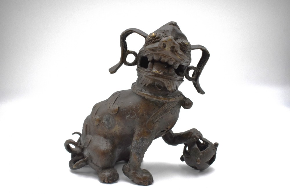 A 17th-century cast bronze Chinese guardian lion figure with an open mouth, pronounced ears, and a paw resting on a pierced sphere.