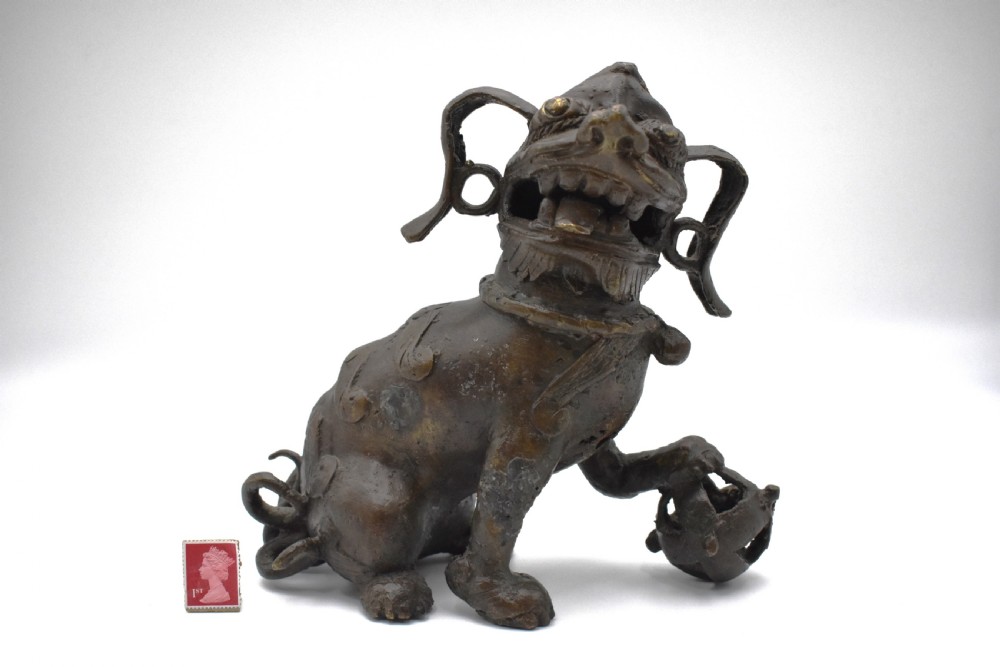 A 17th-century cast bronze Chinese guardian lion figure with an open mouth, pronounced ears, and a paw resting on a pierced sphere. View II