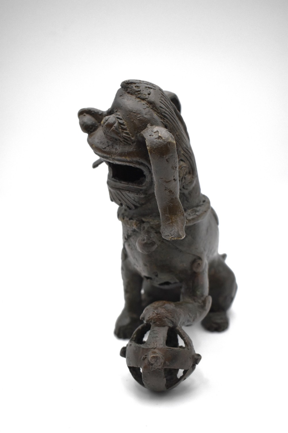 A 17th-century cast bronze Chinese guardian lion figure with an open mouth, pronounced ears, and a paw resting on a pierced sphere. View III