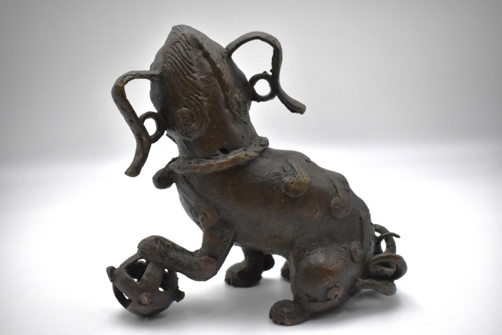 A 17th-century cast bronze Chinese guardian lion figure with an open mouth, pronounced ears, and a paw resting on a pierced sphere. View IV