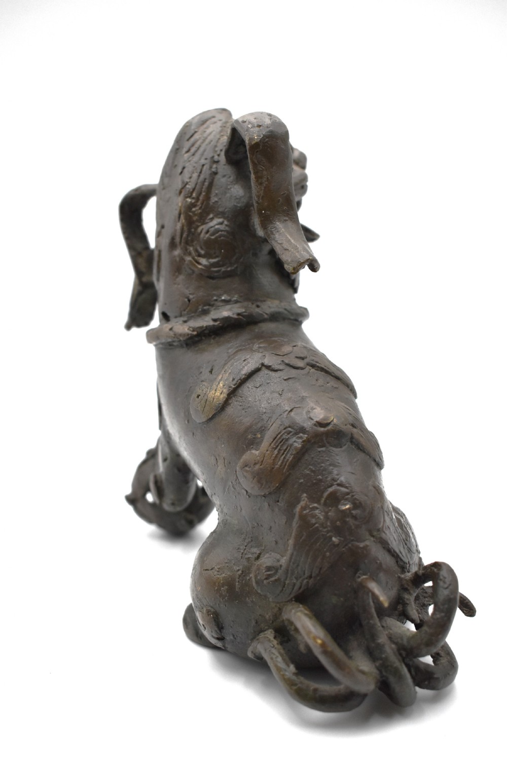A 17th-century cast bronze Chinese guardian lion figure with an open mouth, pronounced ears, and a paw resting on a pierced sphere. View V