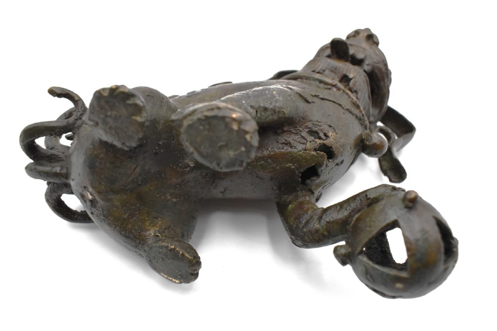 A 17th-century cast bronze Chinese guardian lion figure with an open mouth, pronounced ears, and a paw resting on a pierced sphere. View VII