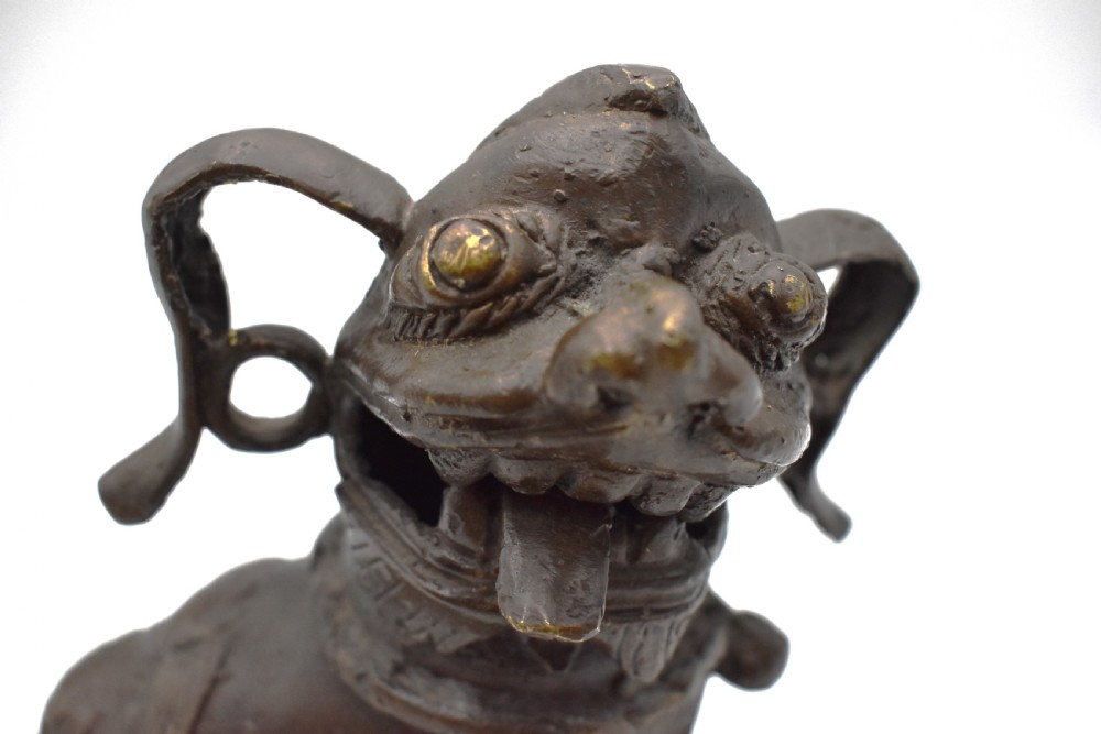 A 17th-century cast bronze Chinese guardian lion figure with an open mouth, pronounced ears, and a paw resting on a pierced sphere. View IX