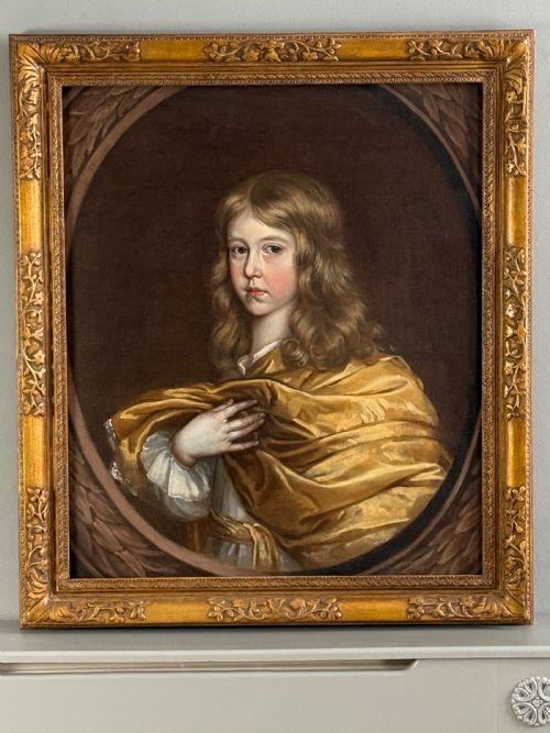 fig 1. A 17th-century oil portrait of a young boy with long curled hair draped in golden-yellow silk, set within a painted trompe loeil oval border.
